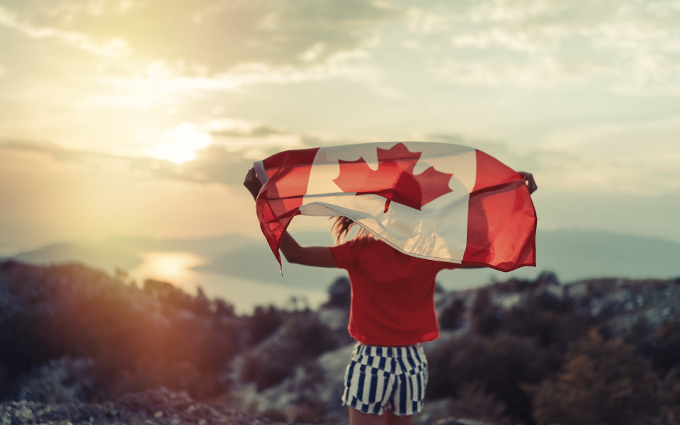 Fr&ouml;hliches Teenagerm&auml;dchen, das beim Laufen bei Sonnenuntergang die Flagge Kanadas schwenkt