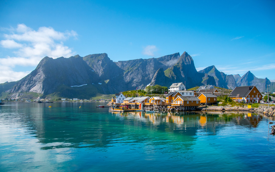 Ein Fischerdorf in der N&auml;he von Reine auf den Lofoten mit traditionellen Holzh&auml;usern am Wasser, umgeben von einer Berglandschaft.