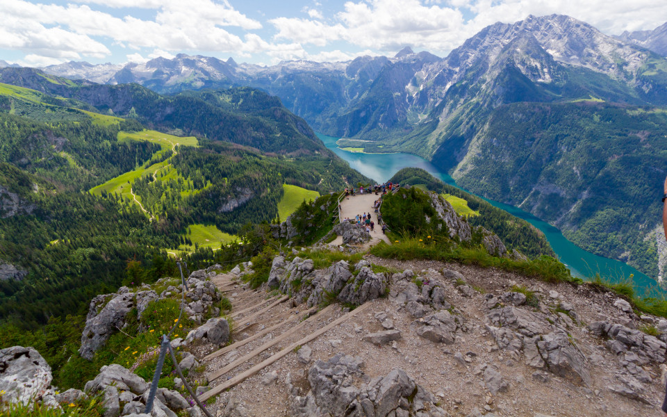 Des Naturparadies K&ouml;nigssee, gesehen vom Jenner aus, mit steilen Bergw&auml;nden, &uuml;ppigem Gr&uuml;n und dem blauen Wasser des Sees im Tal.