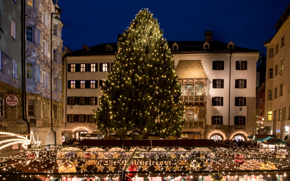 Weihnachtsmarkt in Innsbruck mit gro&szlig;em beleuchtetem Christbaum vor dem Goldenen Dachl in der Altstadt bei Nacht